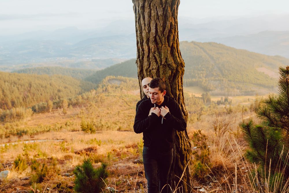 Smiling men hugging near tree in forest on hill