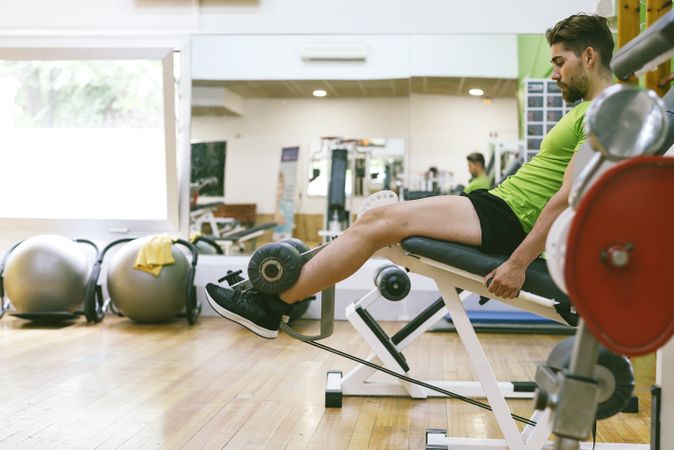 Muscular male in green t-shirt working out using leg extension machine