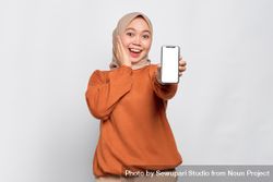 Surprised Muslim woman smiling holding up smartphone with mock up screen 0VQnYb
