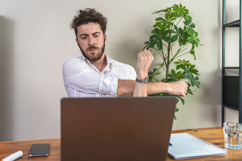 Young man stretching at his office desk during a work break.