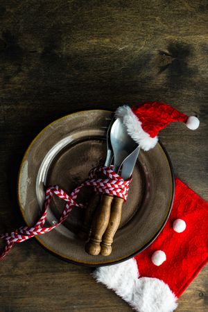 Cutlery setting with red Santa hat on silverware on rustic background, vertical composition