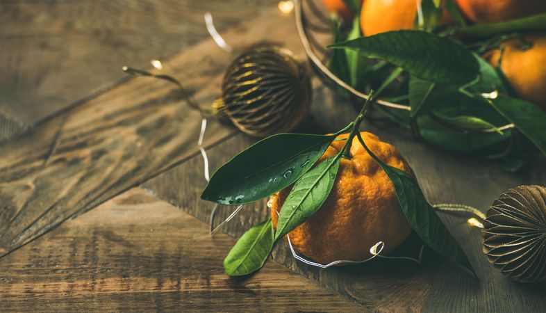 Freshly picked tangerines with leaves on wooden table, with gold Christmas decorations, copy space