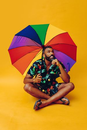 Contemplative Black male thinking about something while sitting under colorful umbrella
