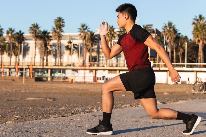 Asian sporty man doing lunges in the beach