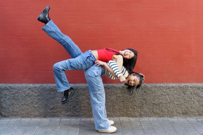 Woman in jeans lifting her smiling friend up on her back