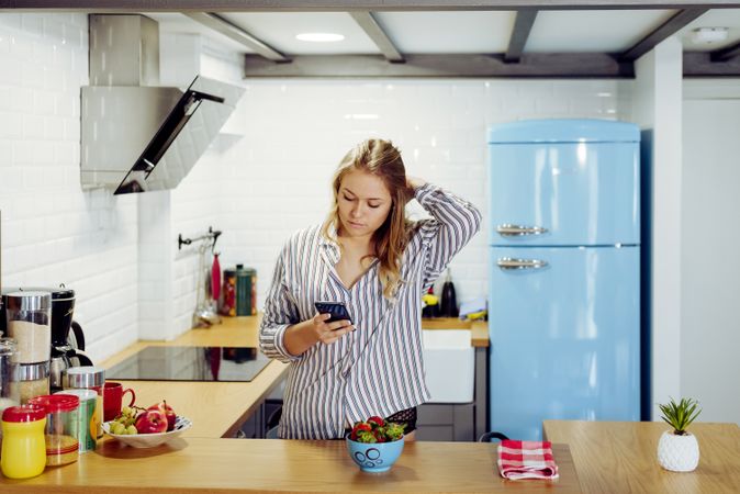 Young female browsing smartphone in kitchen