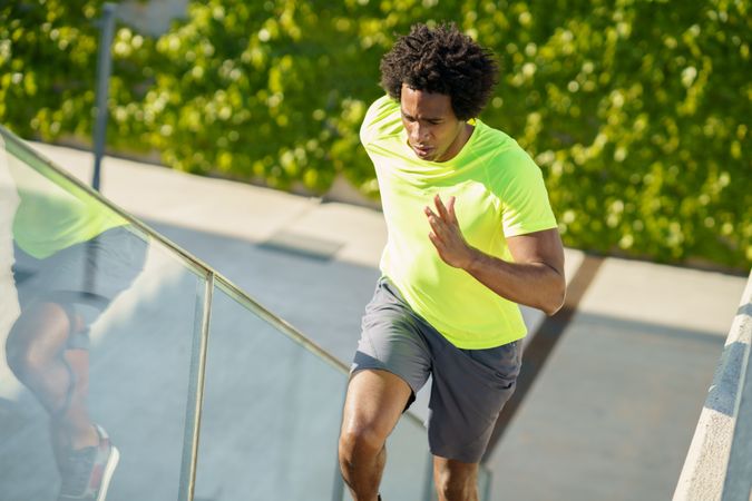 Fit man with afro hair in neon T-shirt jogging up stairs