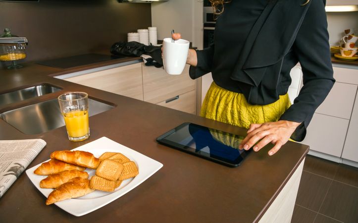 Woman checking tablet while having breakfast at home before work