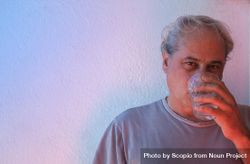 Portrait of middle aged man drinking water against light background in UV lit studio 0KRvZb