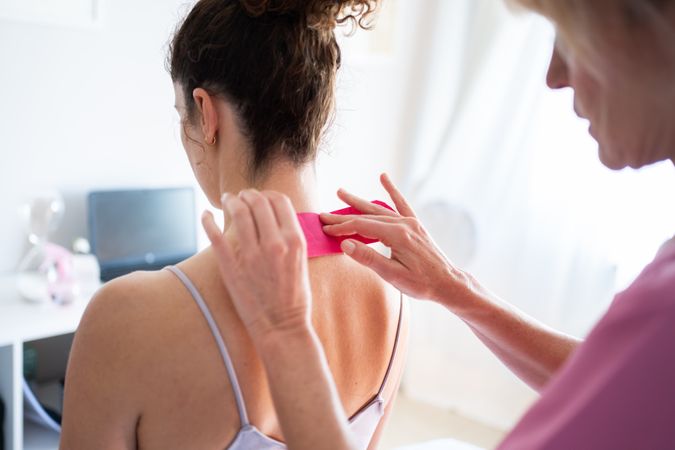 Woman applying soothing kinesiology tape on neck of client