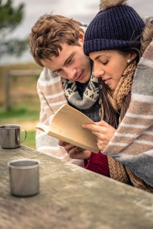 Couple sitting on park bench with coffee cups, making plans on cold autumn day