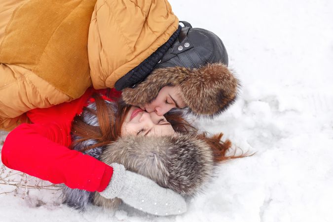 Teenage couple in fur hats kissing on the snow