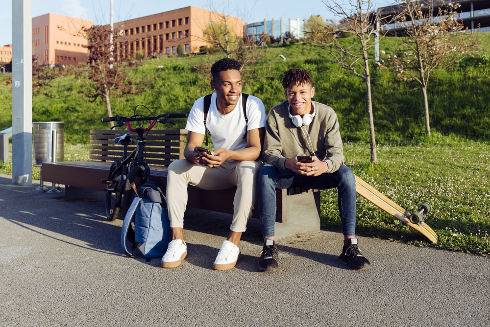 Young Black men sitting on bench with smartphone