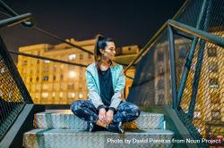 Happy female athlete wearing casual sportswear sitting on a metallic stairs at night 0v3qrg