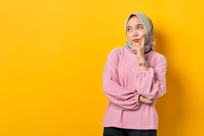 Muslim woman in headscarf thinking deeply about something with hand on chin