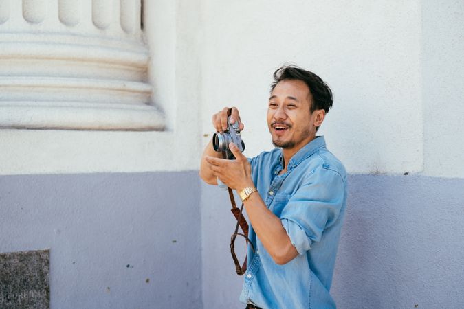 Man with beard laughing while taking photos holding digital camera outside