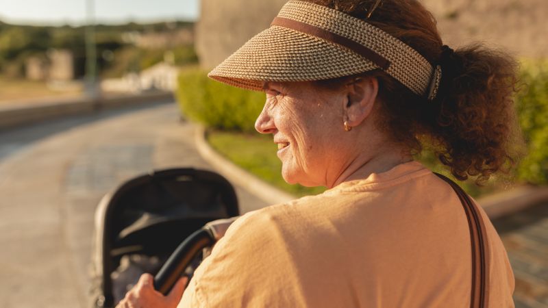 Back of older woman pushing stroller on walk on sunny day
