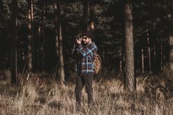 Confident photographer taking picture with camera in sunny forest