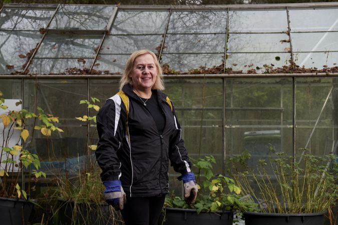 Smiling woman standing with plants outside greenhouse