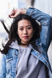 Asian brunette woman with long hair leaning on the wall and looking at camera