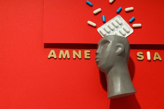 Model of bust with pills on red background and the words “Amnesia” copy space