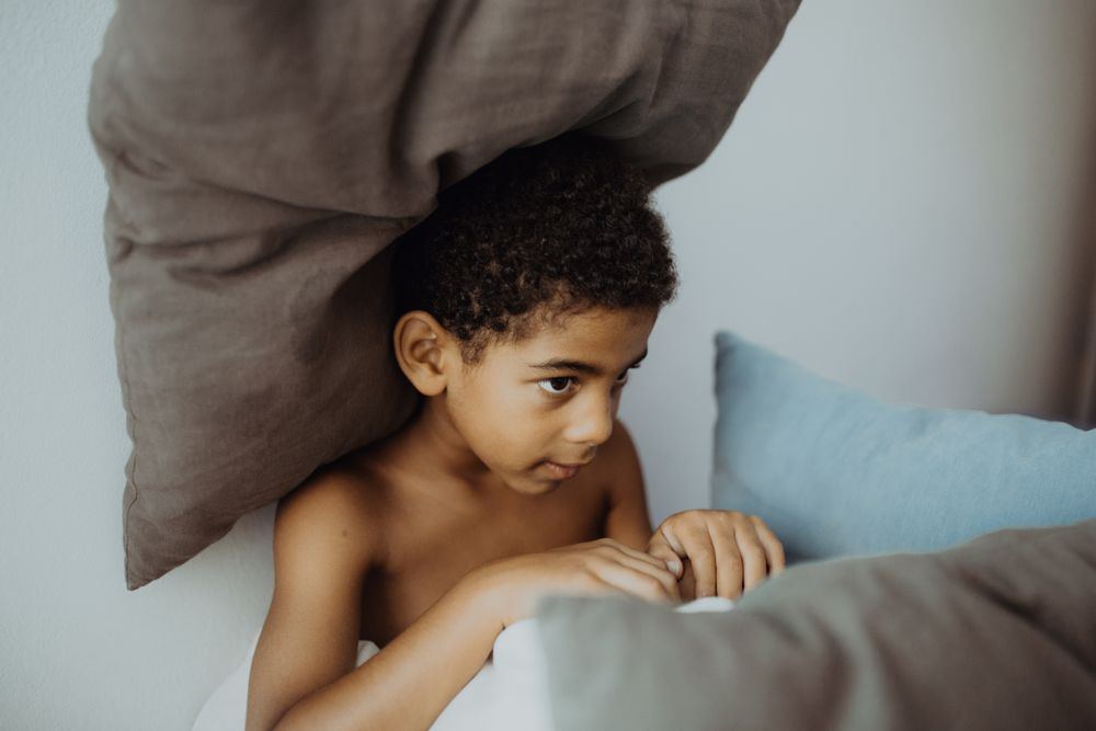 kid lying under pillows