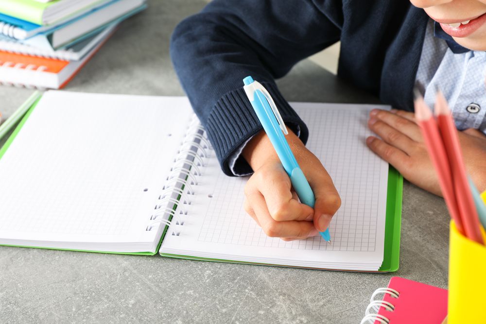 Boy writes in a notebook on grey table, space for text