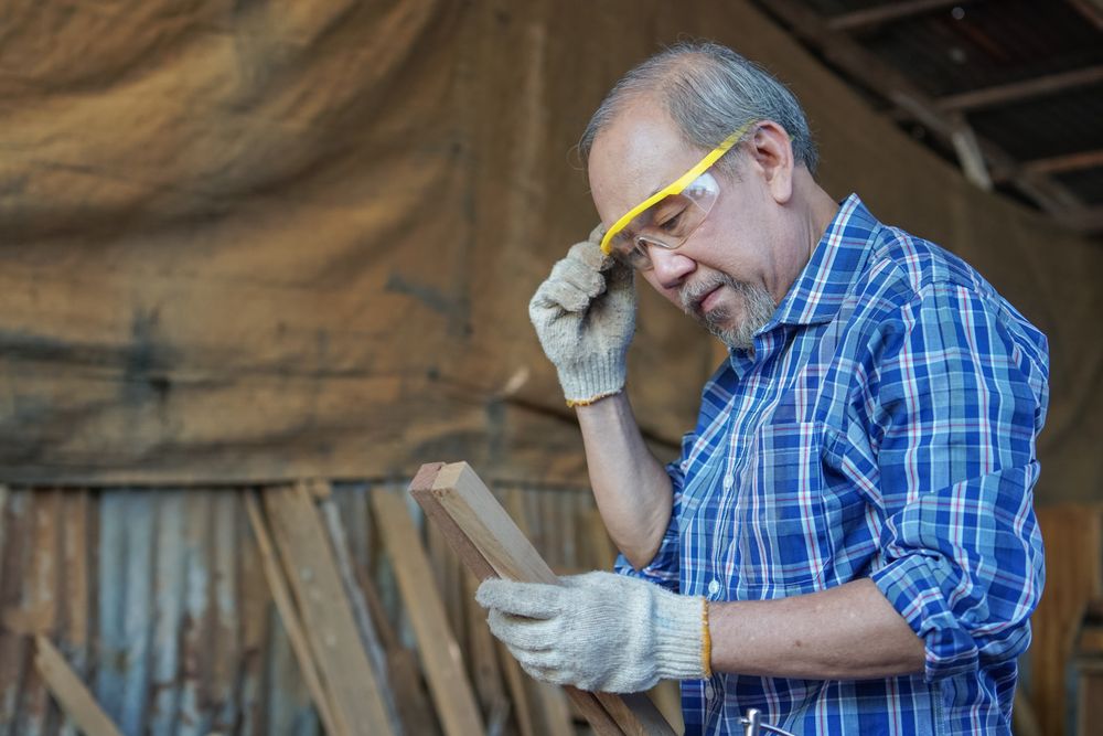 Asian male carpenter picks a wooden panel to work with in shop