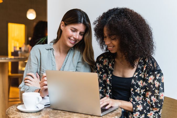 Smiling multiracial girlfriends sharing laptop in coffee shop