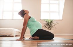 Side view of young pregnant woman kneeling on exercise mat and stretching backwards 5XGOG0