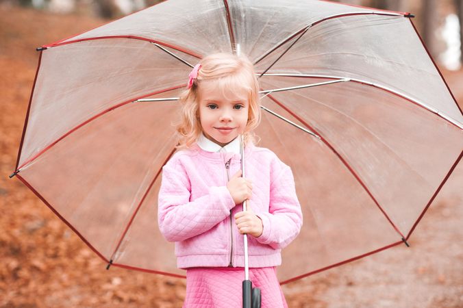 Girl in pink outfit holding an umbrella standing on brown tree leaf