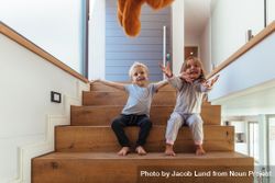 Smiling little kids sitting on stairs and outstretching their hands to catch a teddy bear 49BpQb
