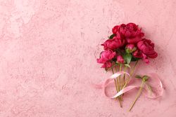 Bouquet of beautiful peonies and pink ribbon on color background, space for text