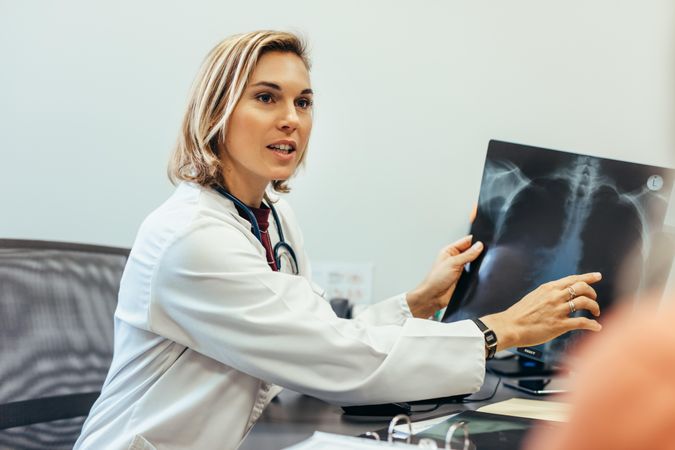 Female doctor showing diagnosis of x-ray image to patient sitting at clinic