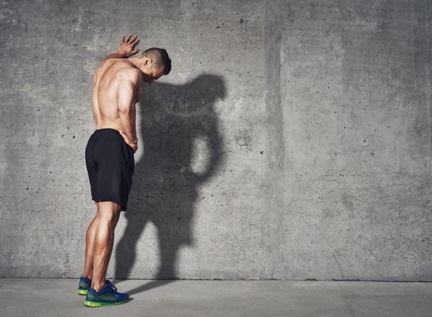 Muscular man in shorts leaning with arm on up wall