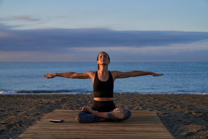 Hispanic woman in lotus pose with spread arms on shore