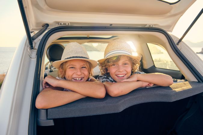 Two smiling children in straw hats leaning in the back seats of