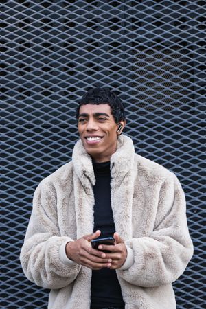 Content stylish man with smartphone in earbud on street