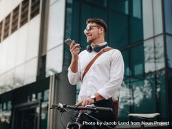 Man holding his bicycle and talking over mobile phone while walking to office 5Qn8E4