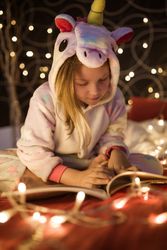 Girl reading book in bedroom decorated with Christmas lights