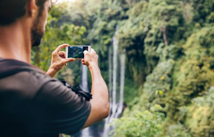 Male hiker photographing a water fall in forest