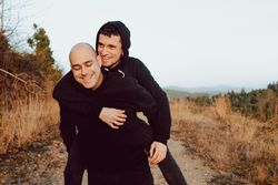 Smiling man holding on back cheerful guy on road on hill