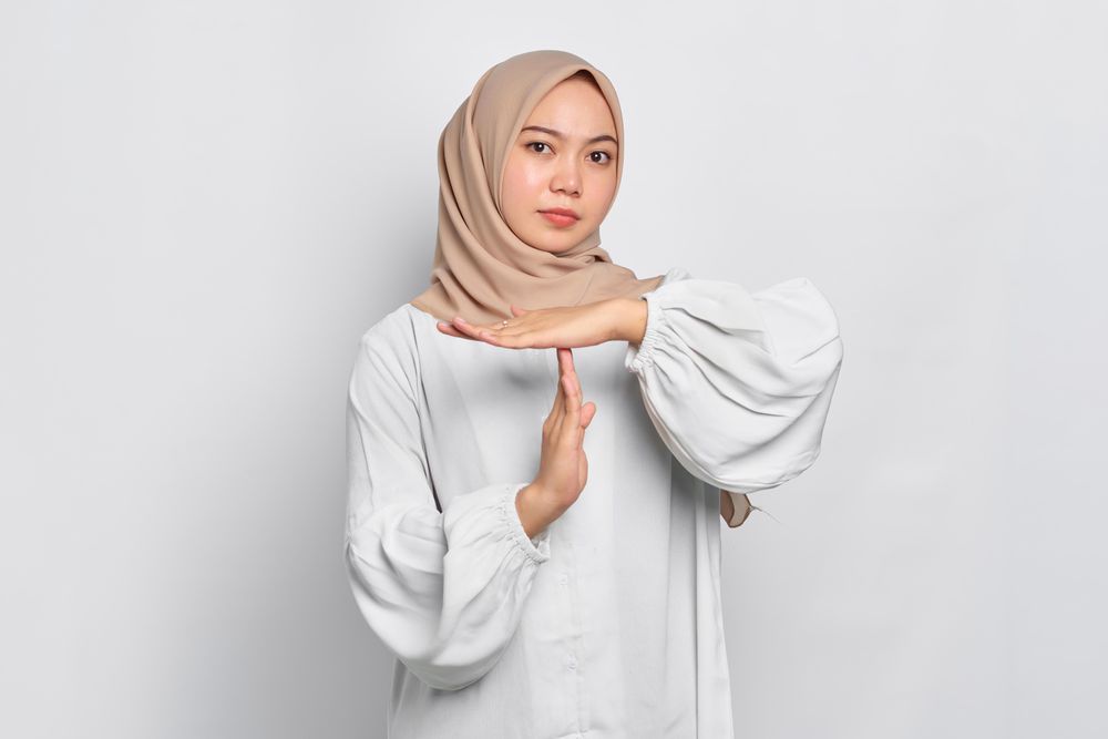 Stern Asian female in headscarf with hands up making “time out” gesture