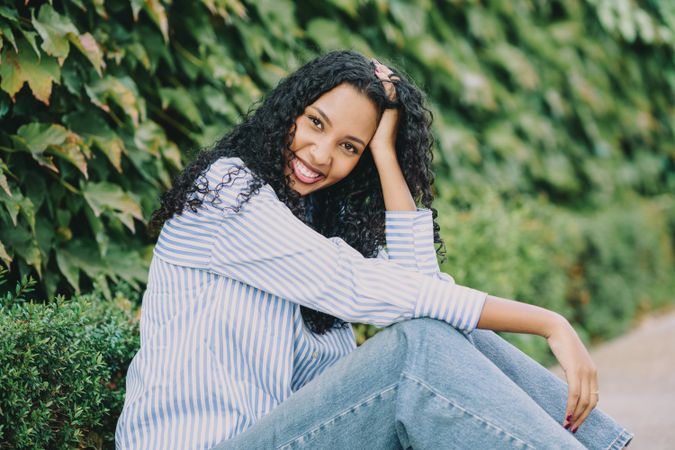 A Joyful Young Woman Sitting Stylishly and Comfortably Among Lush Greenery in the Daylight