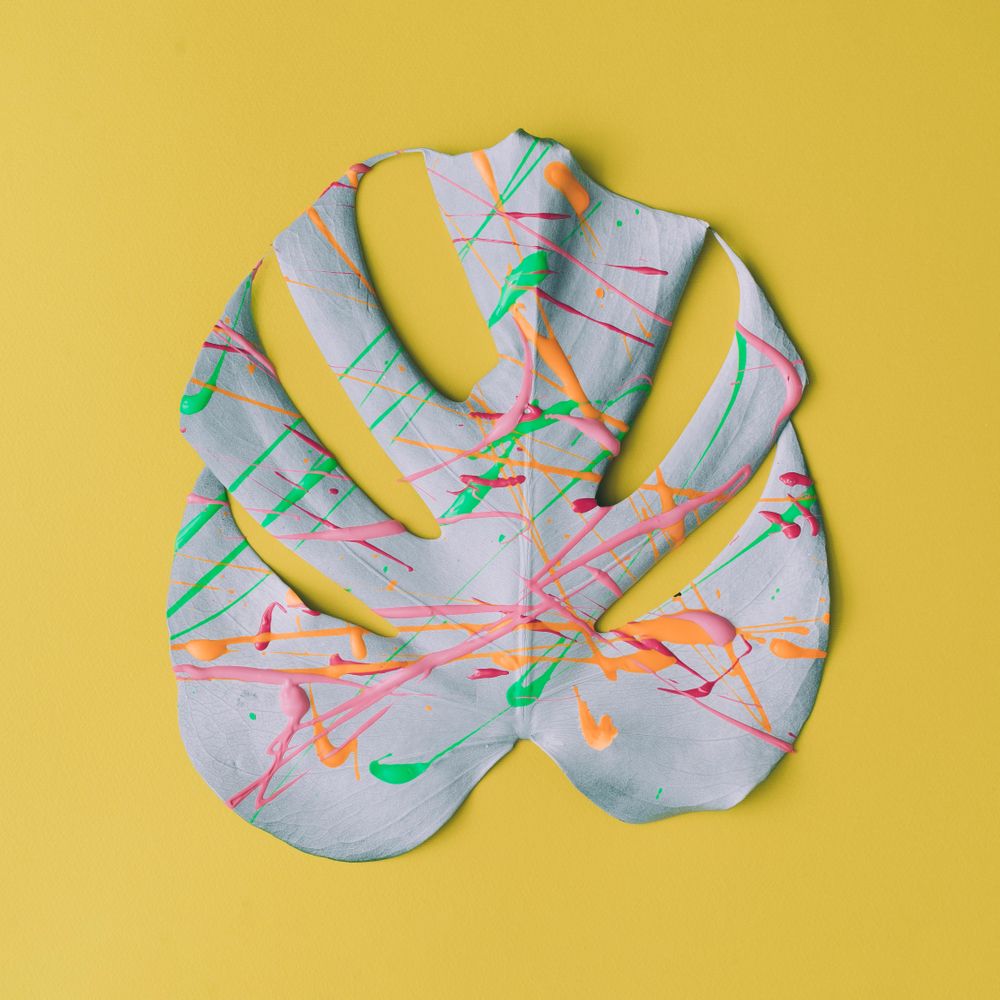 Monstera leaf painted in neon colors on pastel yellow background