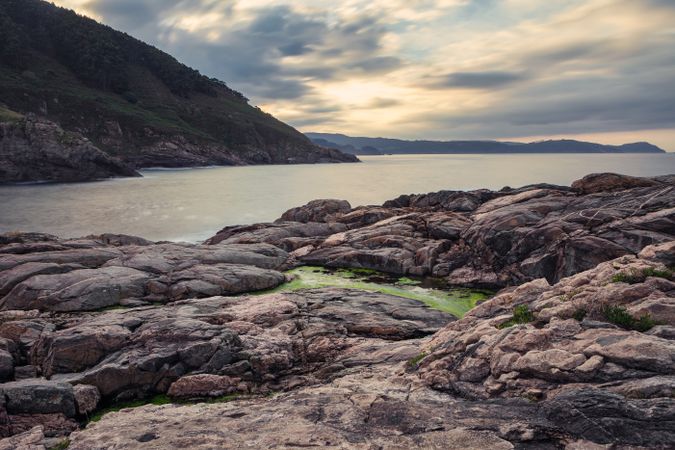 Landscape of rocked seashore with rising sun on cloudy sky