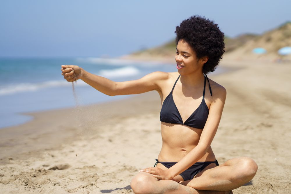 Female in bikini sitting crossed legged in the sand at the beach