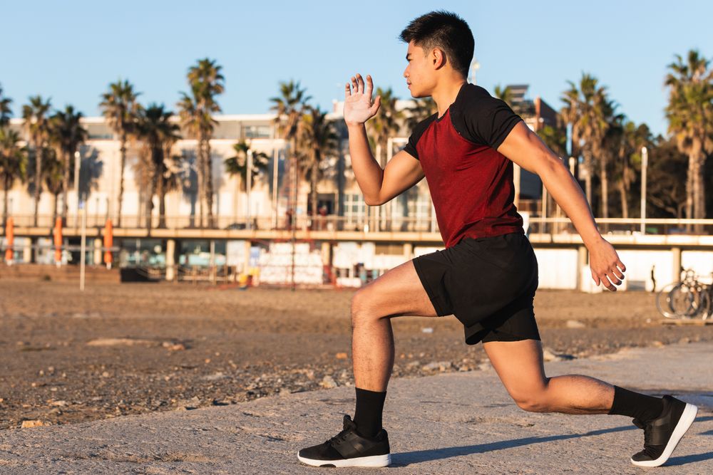 Asian sporty man doing lunges in the beach