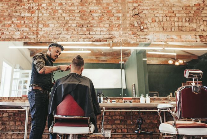 Stylish barber giving haircut to client in barbershop