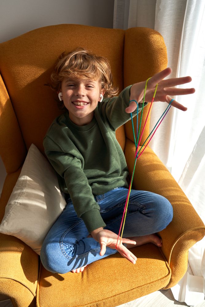Kid with earphones smiling on armchair during string game